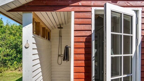 Una cabaña de madera con una pequeña zona de ducha cerrada, una terraza de madera y una puerta que da al interior.