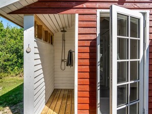 Eine Holzdiele mit einem kleinen, geschlossenen Duschbereich, einer Holzdielen-Terrasse und einer Tür zum Innenraum.