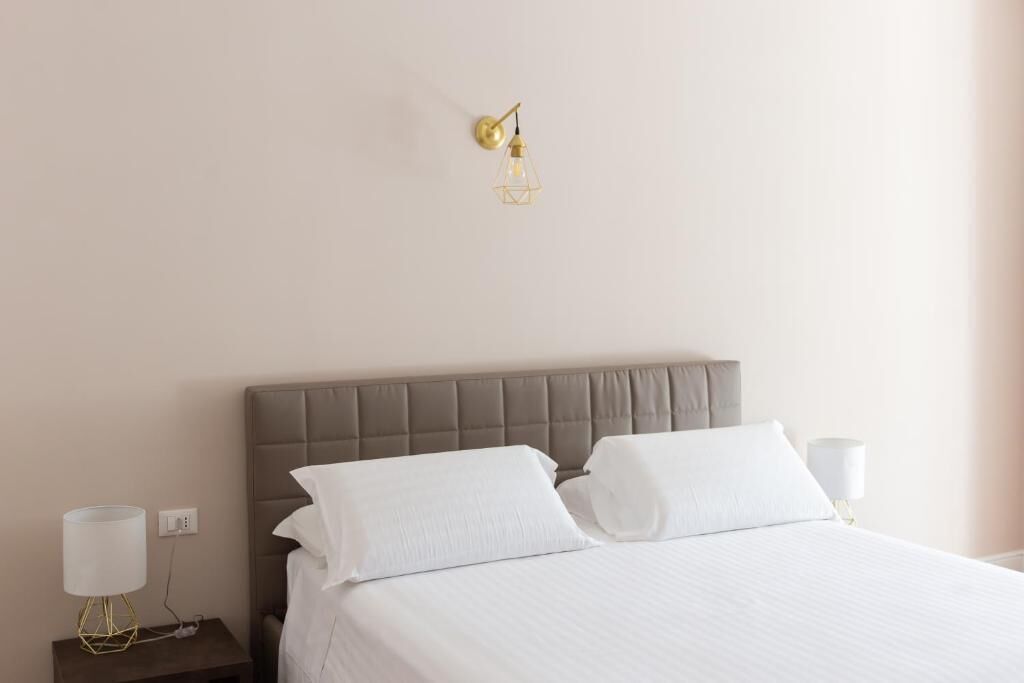 Una cama bien tendida con sábanas blancas y un cabecero gris en una habitación de hotel.