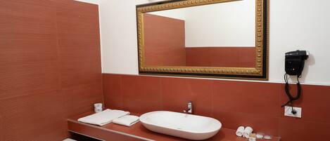 Un baño con un lavamanos blanco, un espejo grande con marco dorado y una pared revestida de baldosas rojas.
