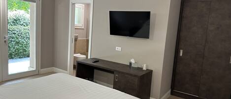 Quarto com cama, cómoda de madeira escura, televisão na parede e porta de acesso a um banheiro.