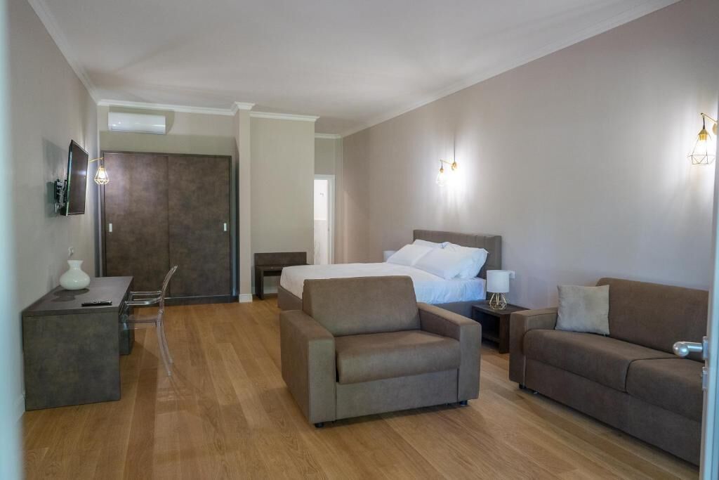 A modern hotel room with a bed, two sofas, a small table, and a TV.