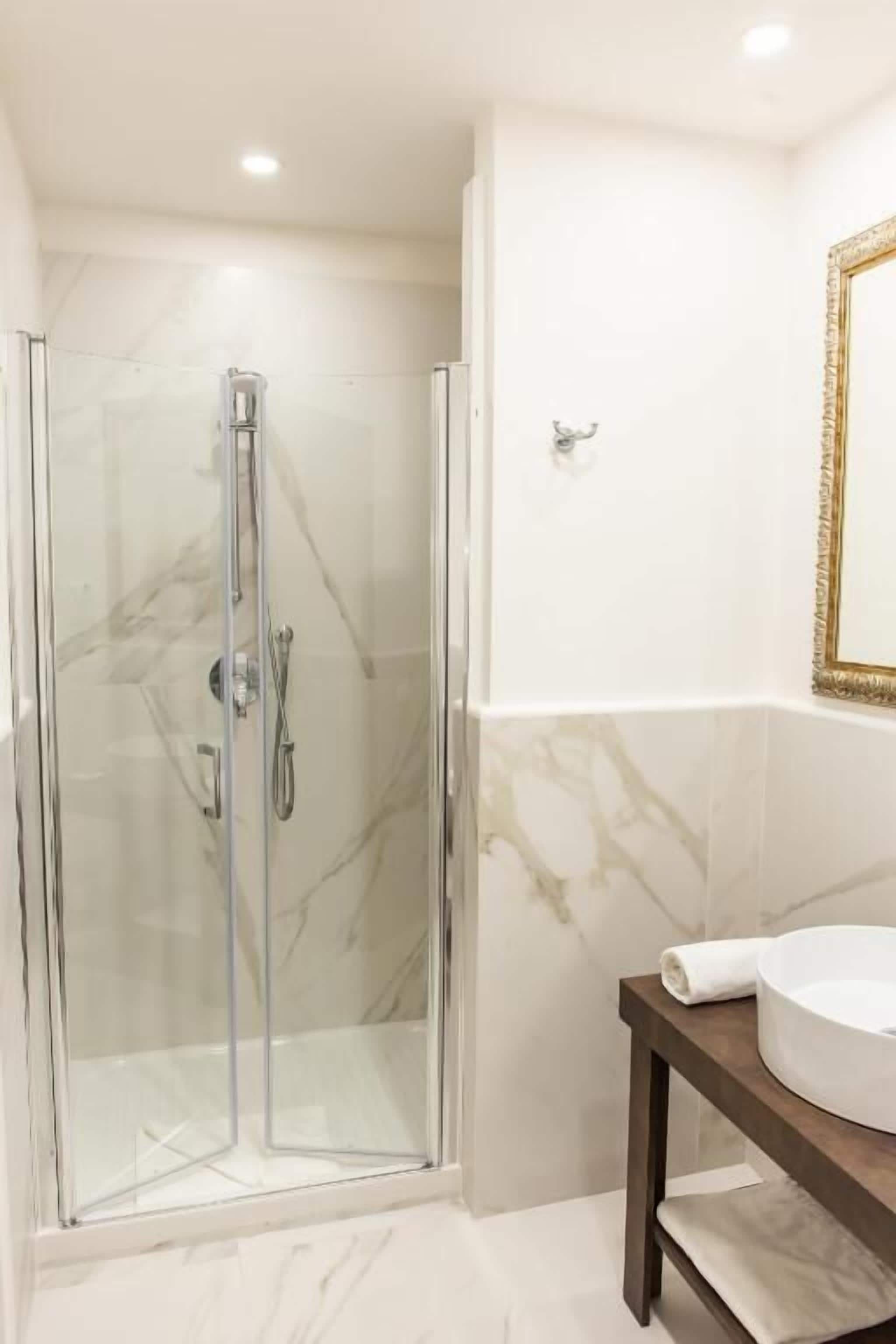 A glass-enclosed shower with a handheld showerhead and a wall-mounted faucet.
