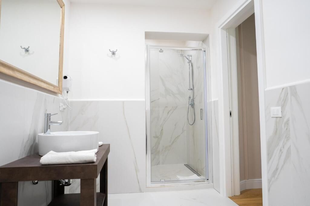 A modern bathroom with a marble sink, a glass shower enclosure, and a wooden vanity.