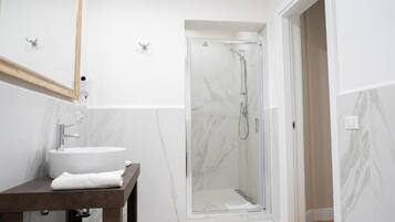 Un baño moderno con lavamanos de mármol, cabina de ducha de vidrio y tocador de madera.