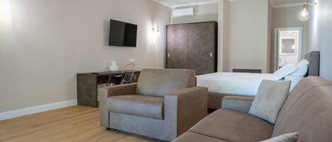 Quarto de hotel moderno com uma cama grande, um sofá, uma escrivaninha e uma TV fixada na parede.