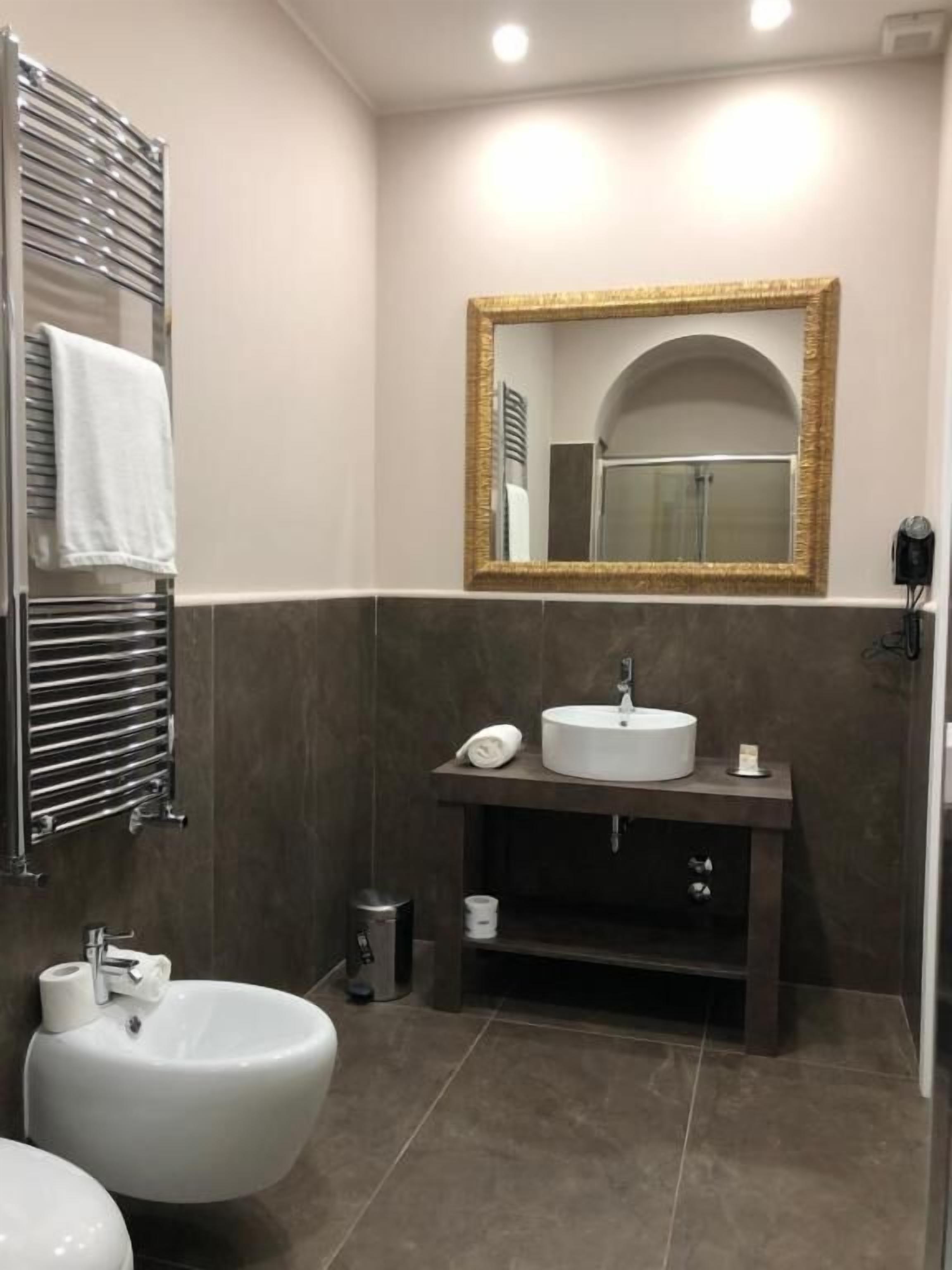 A modern bathroom with a large mirror, a round sink, a bidet, and a towel rack.