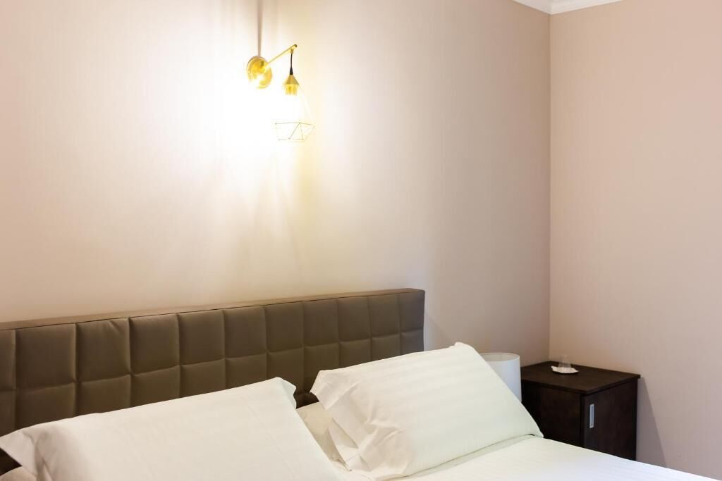 A hotel room with a bed, a nightstand, and a wall-mounted light fixture.