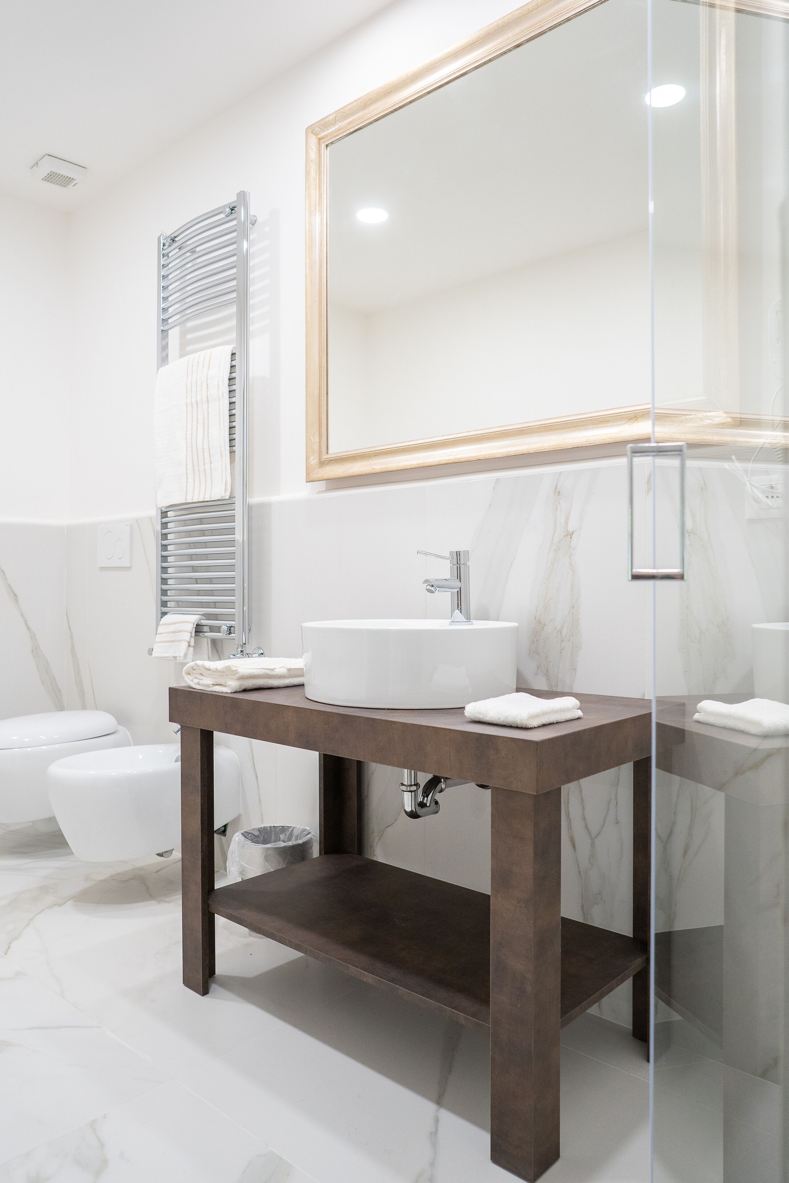 A modern bathroom with a large mirror, a white sink, and a dark wooden vanity.