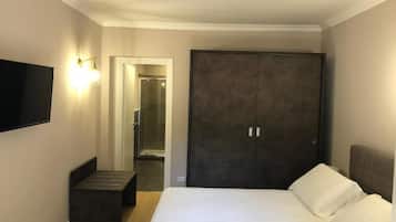 Une chambre d’hôtel avec un lit, une armoire sombre, un banc et un téléviseur à écran plat fixé au mur.