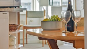 Un coin repas avec une table dressée pour deux personnes, agrémenté d’un saladier de raisins verts et de deux verres à vin, d’une bouteille de vin et d’un four à micro-ondes posé sur le comptoir.