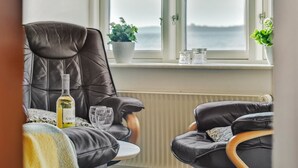 Une pièce chaleureuse avec un fauteuil en cuir, une petite table sur laquelle se trouvent une bouteille et des verres, et une fenêtre donnant sur la mer.