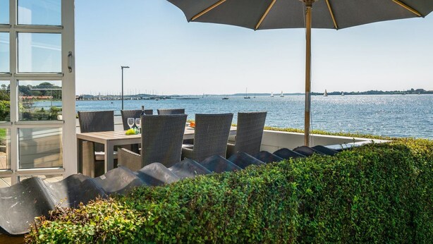 Une terrasse en bord de mer avec des sièges extérieurs, un grand parasol et une vue sur la mer.