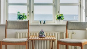 Une pièce avec deux chaises en bois et une petite table, un radiateur blanc et une fenêtre donnant sur la mer.