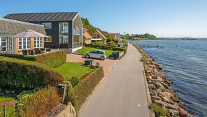 Un quartier résidentiel situé sur la côte, avec des maisons modernes, une promenade pavée le long de l’eau et une vue dégagée sur la mer.