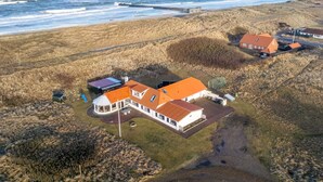 Vue aérienne d’une propriété située sur la côte, avec une grande maison dotée d’un toit recouvert de tuiles rouges, d’un patio circulaire et d’une vue sur l’océan.