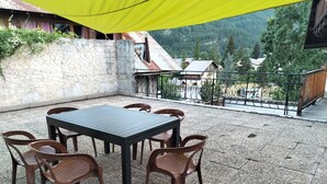 An outdoor patio with a table and chairs, a yellow canopy, and a view of houses and mountains in the background. - Maison Classée 1 Étoile (Vallouise-Pelvoux)