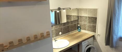 A compact bathroom with a wooden vanity, a sink, a mirror, a towel rack, a washing machine, and a shower curtain.