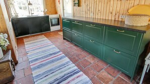 A kitchen with wooden walls, green cabinets, a striped rug, and a window overlooking a garden.