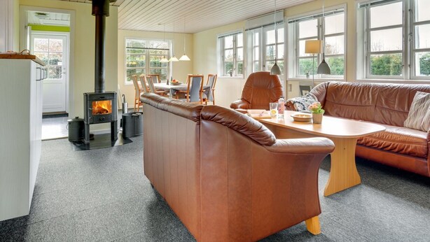 A modern living room with a fireplace, leather sofa, dining area, and large windows. - "Swaver" - 300m to the fjord by Interhome (Storvorde)