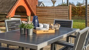 A wooden outdoor dining area with a table and chairs, a metal pitcher, a tray with plates and cups, and a small garden. - "Swaver" - 300m to the fjord by Interhome (Storvorde)