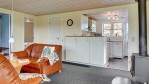 A cozy living room with a brown leather sofa, a dining table, and a kitchen area with white cabinets and a black stove. - "Swaver" - 300m to the fjord by Interhome (Storvorde)