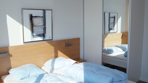 A bedroom with a wooden headboard, a bed with white bedding, a bedside table, and a wall-mounted mirror. - "Fanny" - 2km from the sea by Interhome (Rømø)