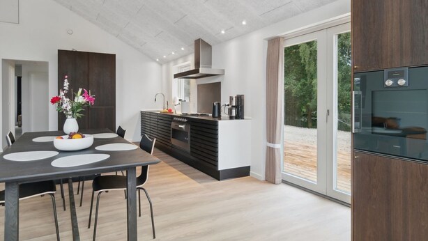Cocina moderna con zona de comedor, que incluye una isla central, muebles oscuros y un amplio ventanal con vistas al exterior.