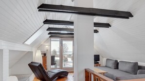 Un dormitorio tipo loft moderno con techo inclinado, un banco empotrado, sofá gris y suelo de madera.