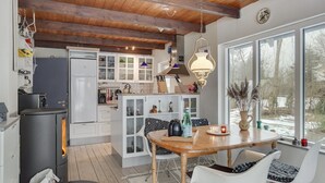 Una cocina moderna con vigas de madera, armarios blancos y un comedor con mesa de madera y sillas blancas.