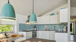 Une cuisine moderne avec des meubles blancs, un dosseret en carreaux bleus et des luminaires suspendus.