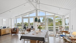 Une pièce spacieuse et bien éclairée, dotée d’une grande table à manger, de sièges confortables et de larges fenêtres offrant une vue sur l’extérieur.