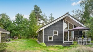 Une maison à deux étages, à l’extérieur sombre, dotée d’un patio couvert avec des meubles d’extérieur et d’une pelouse bien entretenue.
