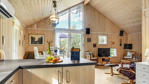 Une cabane spacieuse avec un plafond haut, des murs en bois, une grande cuisine avec un îlot central, un coin repas avec un téléviseur et un coin salon confortable avec une cheminée.