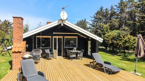 A wooden deck with outdoor furniture, a brick chimney, and a modern building with large windows and a satellite dish. - "Weland" - 800m from the sea by Interhome (Løkken)