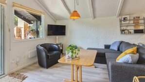 A modern living room with a grey sofa, a black leather chair, a wooden coffee table, and a TV mounted on the wall. - "Weland" - 800m from the sea by Interhome (Løkken)