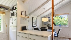 A compact kitchen with a white refrigerator, microwave, and a small countertop. There is a dining area with a table and chairs, and a window providing a view of greenery outside. - "Weland" - 800m from the sea by Interhome (Løkken)