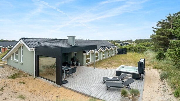 Una casa moderna con un porche cubierto, mobiliario exterior y un jacuzzi.
