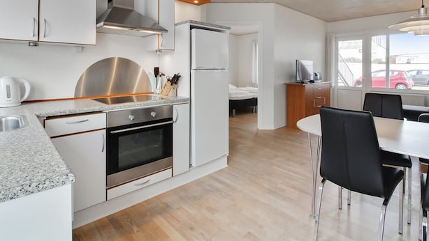 A modern kitchen with white cabinetry, stainless steel appliances, and a dining area with black chairs. - "Haghni" - 200m from the sea by Interhome (Løkken)
