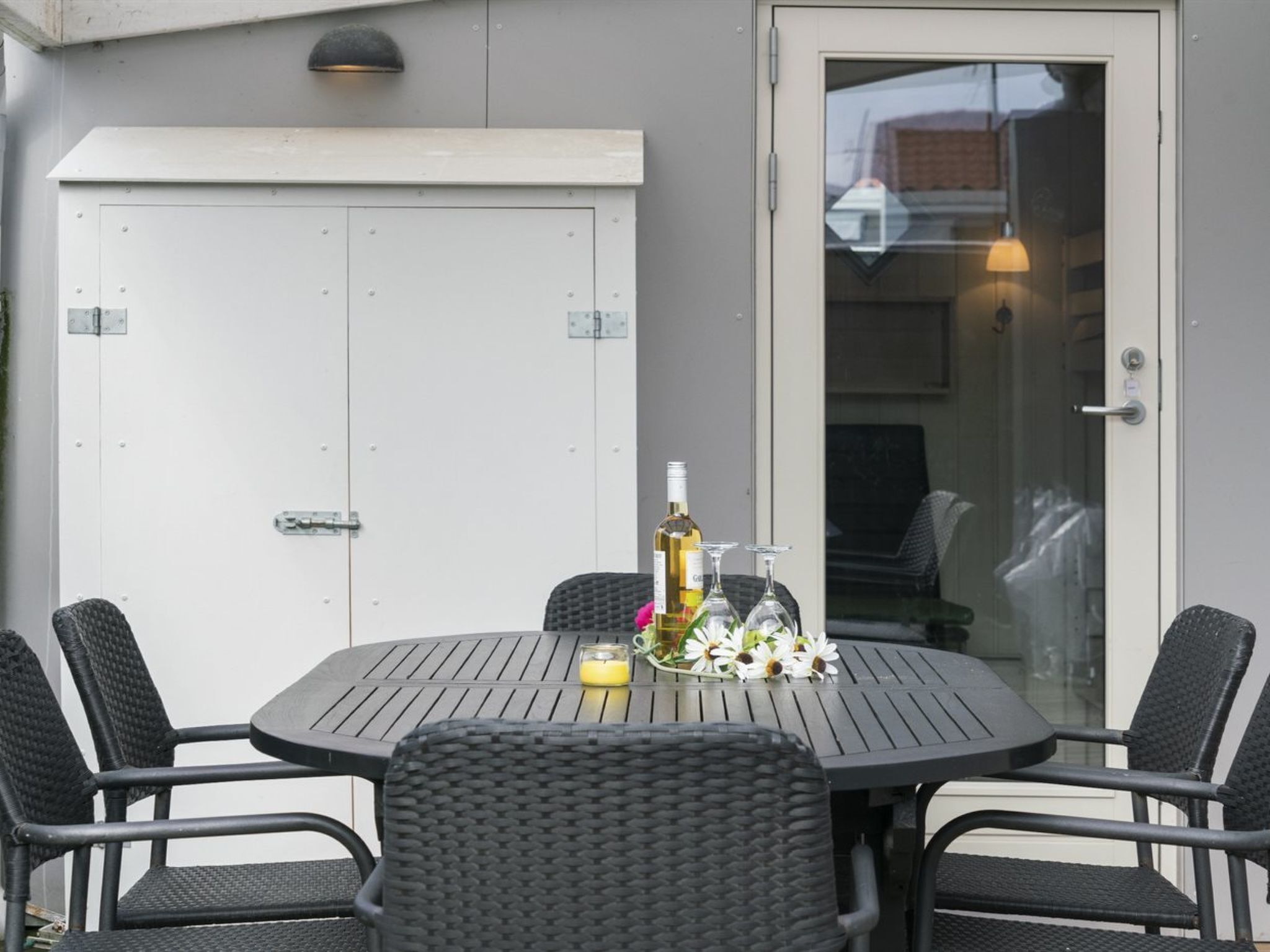 A round table with four wicker chairs, a bottle of wine, and a candle on the table.