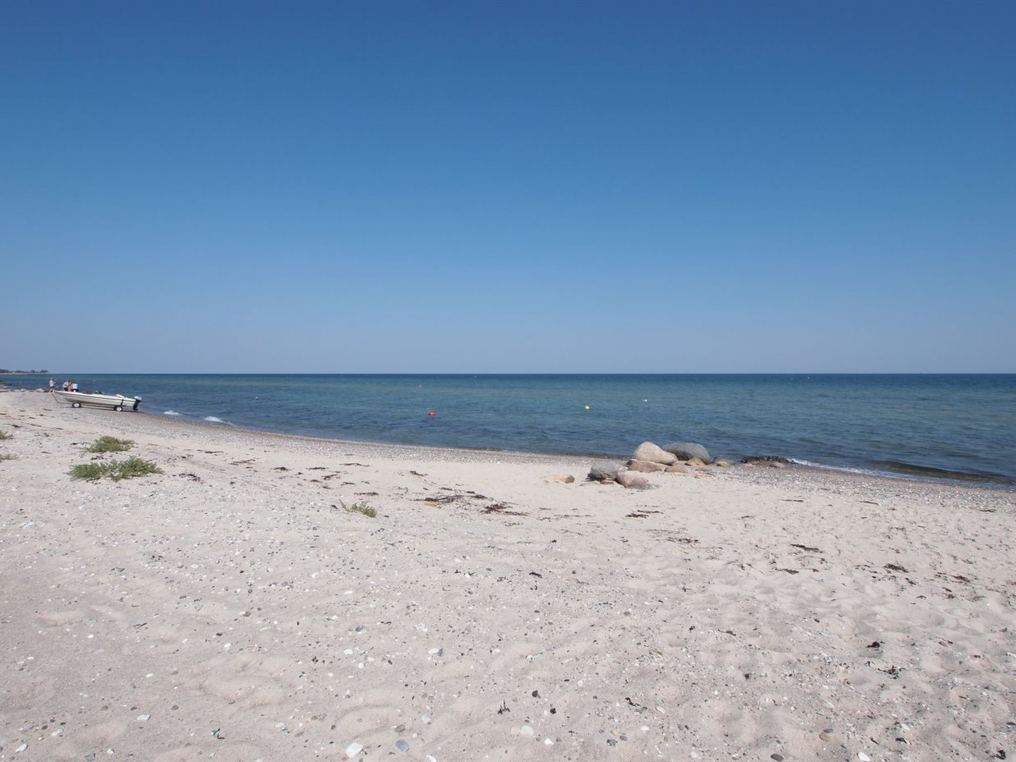 Een strand met een boot in het zand, een helderblauwe lucht en een rustige zee.