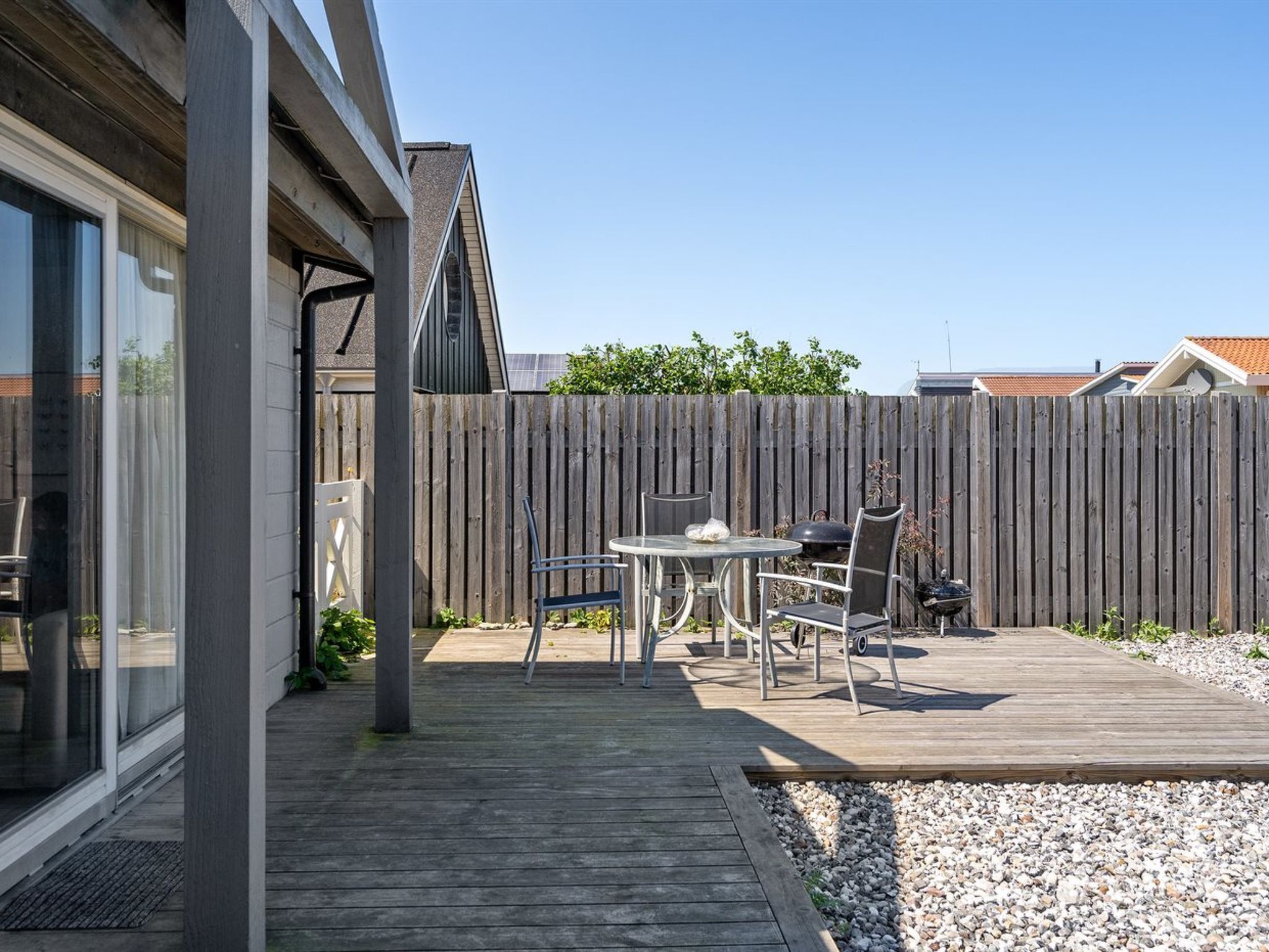 Une terrasse moderne avec une plateforme en bois, une porte d’entrée en verre et une table entourée de chaises.