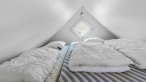 A small, triangular attic bedroom with a skylight, a bed with white and striped bedding, and a single nightstand. - "Poulsen" - 200m from the sea by Interhome (Løkken)