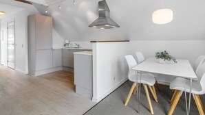 A modern kitchen with white cabinetry, a built-in oven, and a coffee machine. There is a dining area with a white table and chairs, and a small plant on the table. - "Poulsen" - 200m from the sea by Interhome (Løkken)