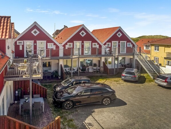 A row of red-roofed houses with balconies, a car parked in front, and a clear sky.