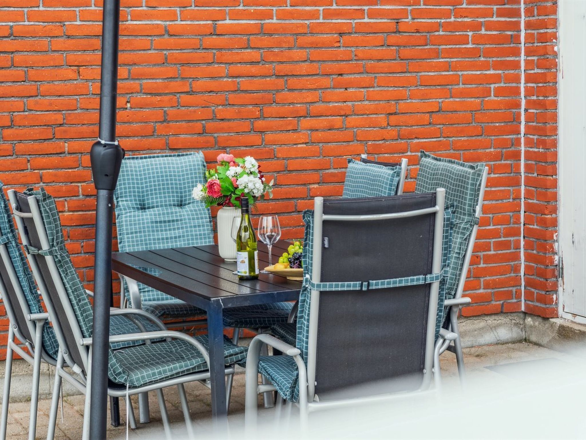 An outdoor patio with a brick wall, a table, chairs, and a bottle of wine.