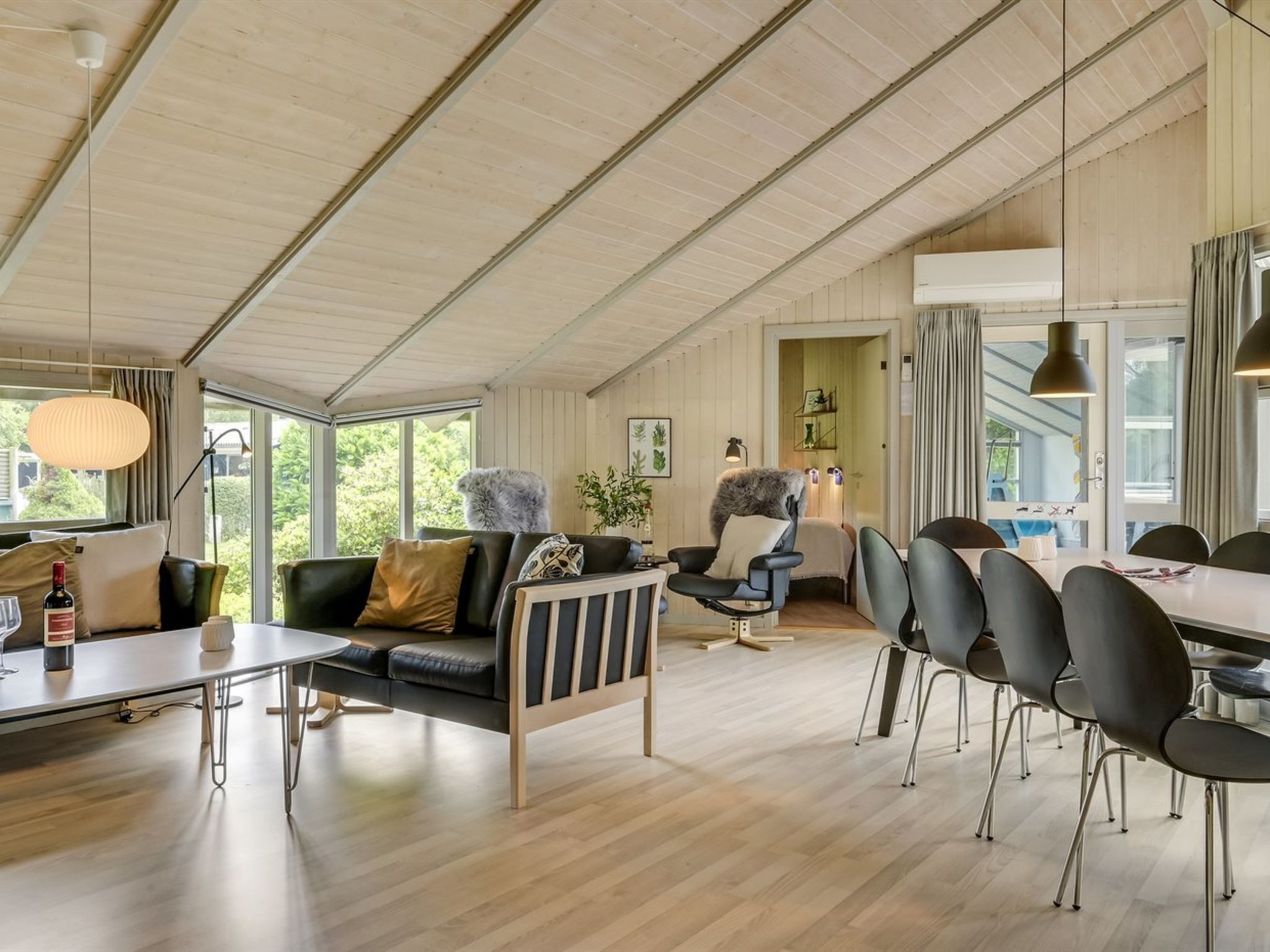 Un vaste espace de vie doté d’un haut plafond, une table à manger avec des chaises, un canapé et un fauteuil agrémenté d’un plaid en fourrure.