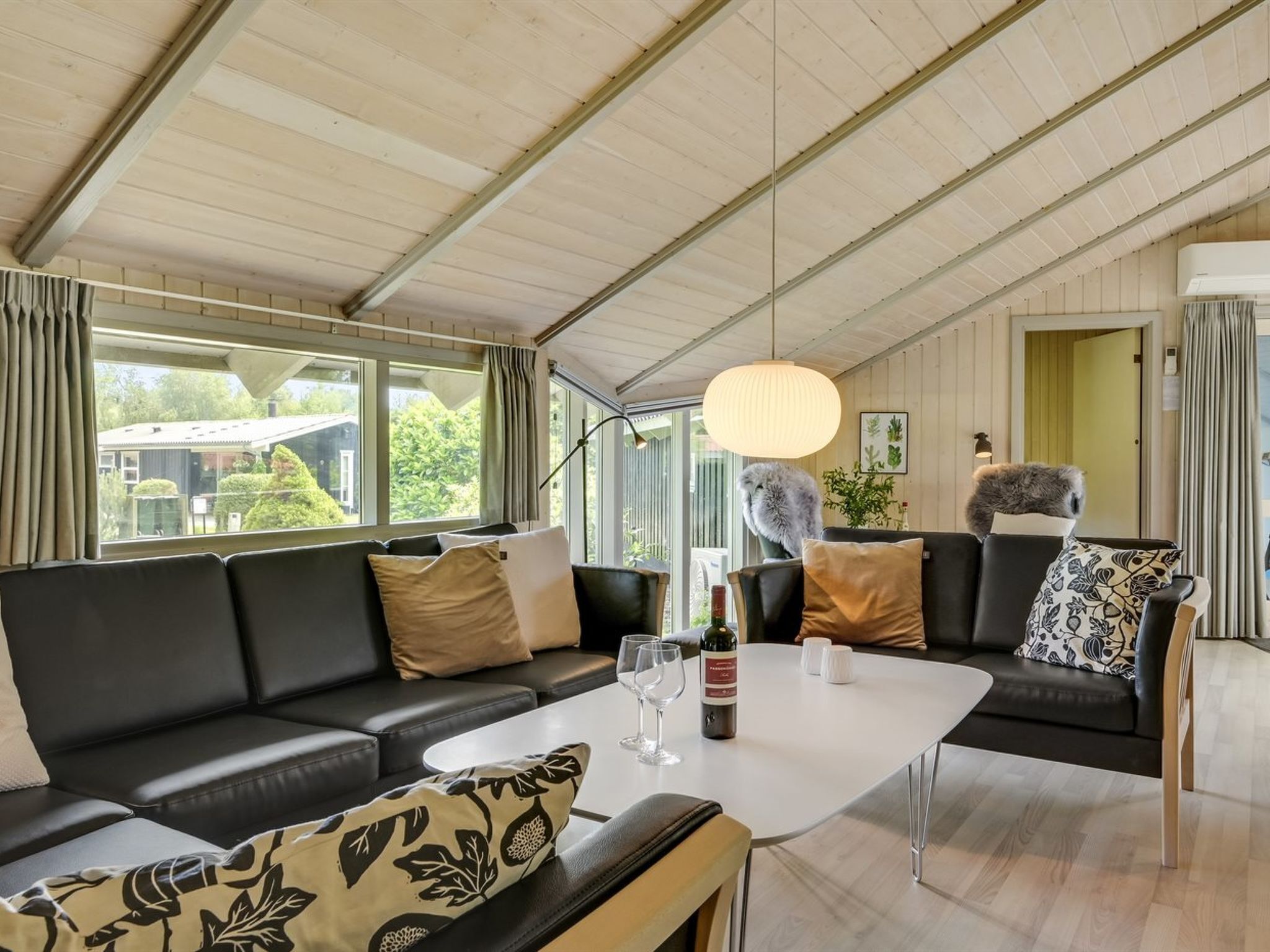 Un salon moderne avec un canapé en cuir noir, une table basse blanche et une grande fenêtre donnant sur un paysage verdoyant.