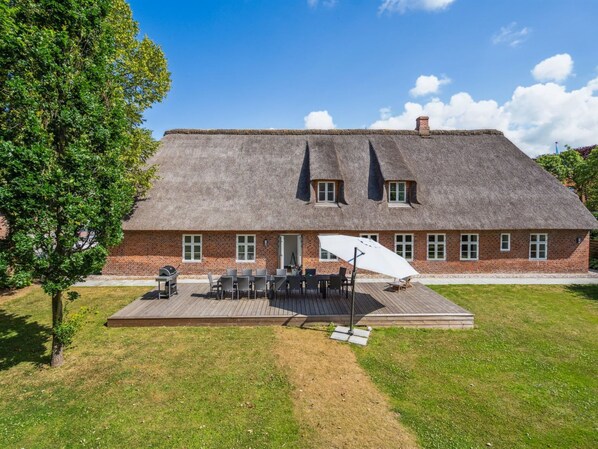 A thatched-roof house with a brick exterior, a deck with outdoor furniture, and a lawn.