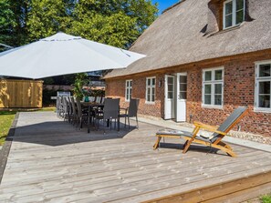 A wooden deck with a table and chairs, a thatched-roof building, and a lounge chair.